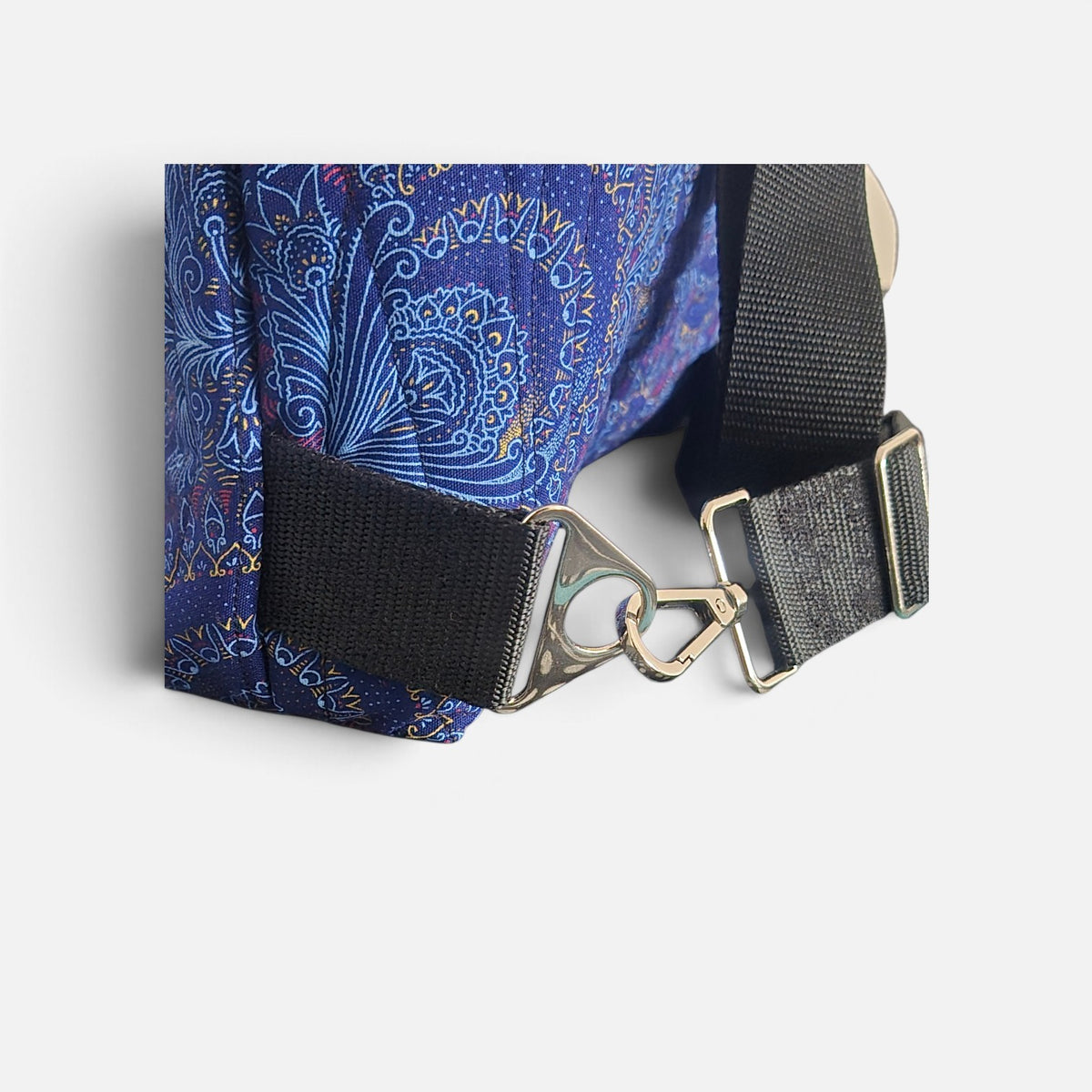 Close-up of blue Shweshwe fabric, black webbing strap, silver-tone swivel clip and adjuster.