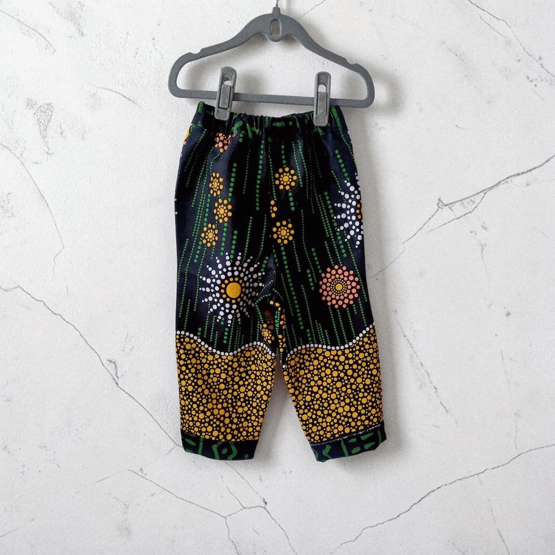 Big Bag Maker Sunburst trousers featuring a black fabric with vibrant yellow, orange, and white dot art patterns.