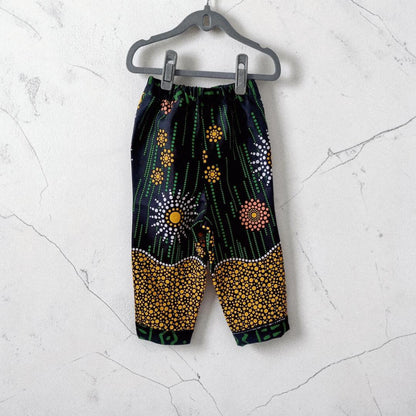 Big Bag Maker Sunburst trousers featuring a black fabric with vibrant yellow, orange, and white dot art patterns.