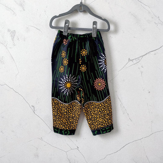 Big Bag Maker Sunburst trousers featuring a black fabric with vibrant yellow, orange, and white dot art patterns.