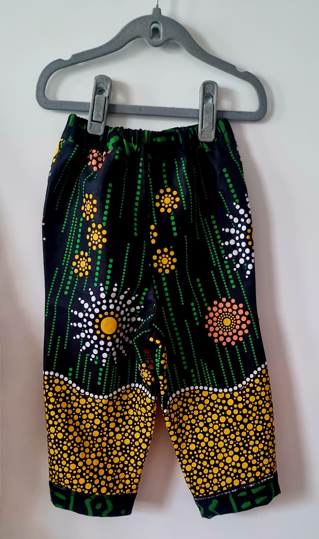 Big Bag Maker Sunburst trousers featuring a black fabric with vibrant yellow, orange, and white dot art patterns.