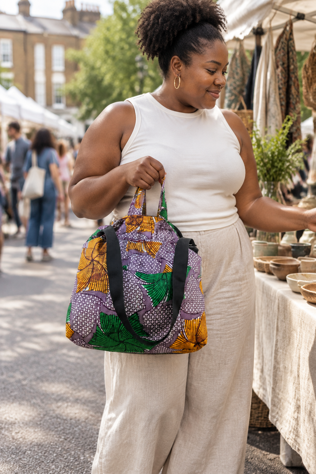 Model carrying the purple, yellow and green Fans and Dots market bag by its fabric handles at an outdoor market.