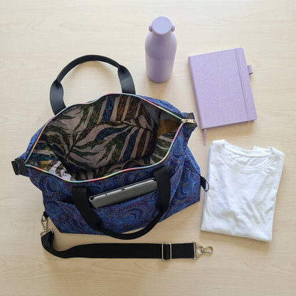Open Blue Peacocks Traveller showing its leaf-print lining, with a detachable black strap, lavender bottle, notebook and folded white T-shirt arranged beside it.